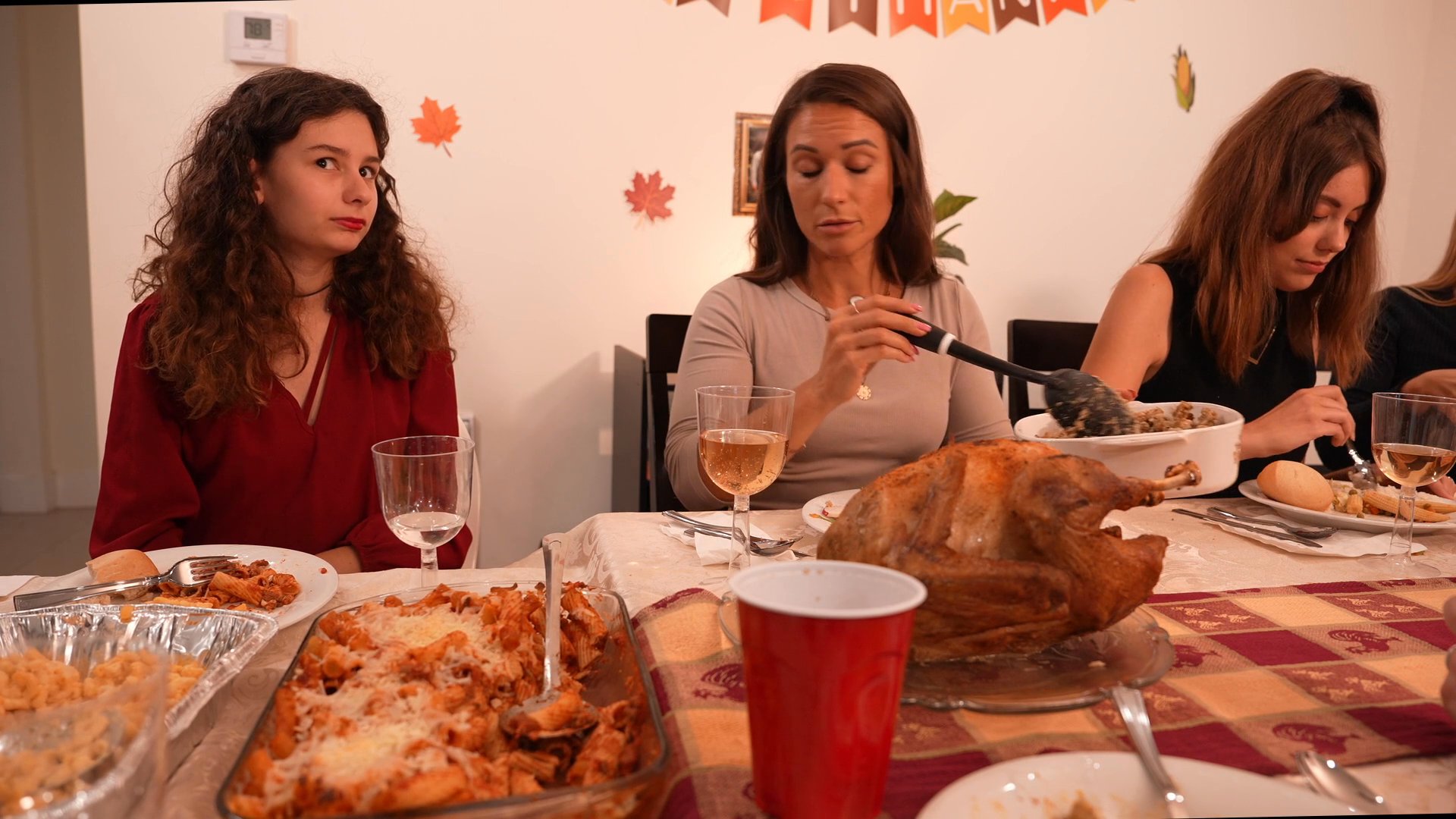 A group of adults enjoys a traditional Thanksgiving meal together, passing dishes and engaging in conversation around a festive table.
