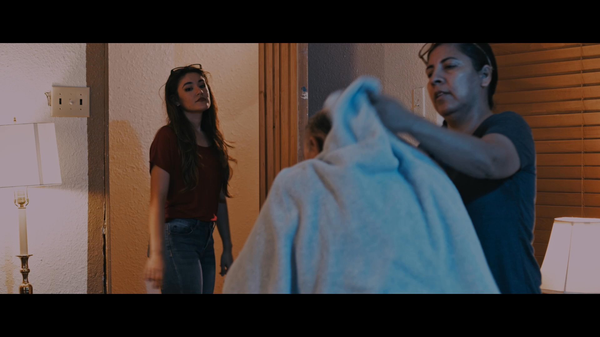 Family caregivers assist an elderly man by drying his hair with a towel to ensure his comfort and health. The scene captures a moment of attentive, compassionate support within a home environment.