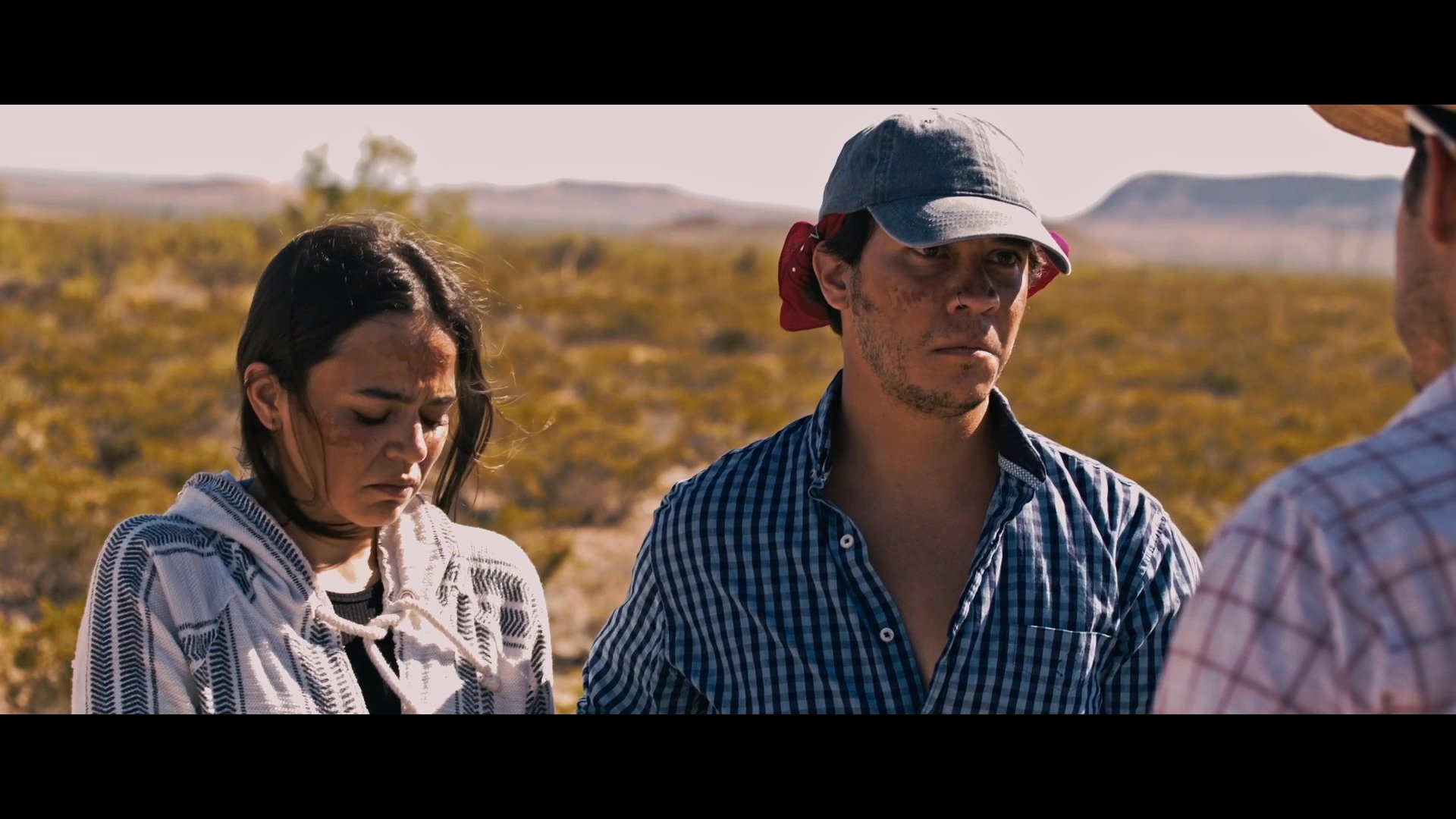 A group of individuals in a desert setting engage in a tense confrontation where one person is pressured into offering an apology for a false accusation.