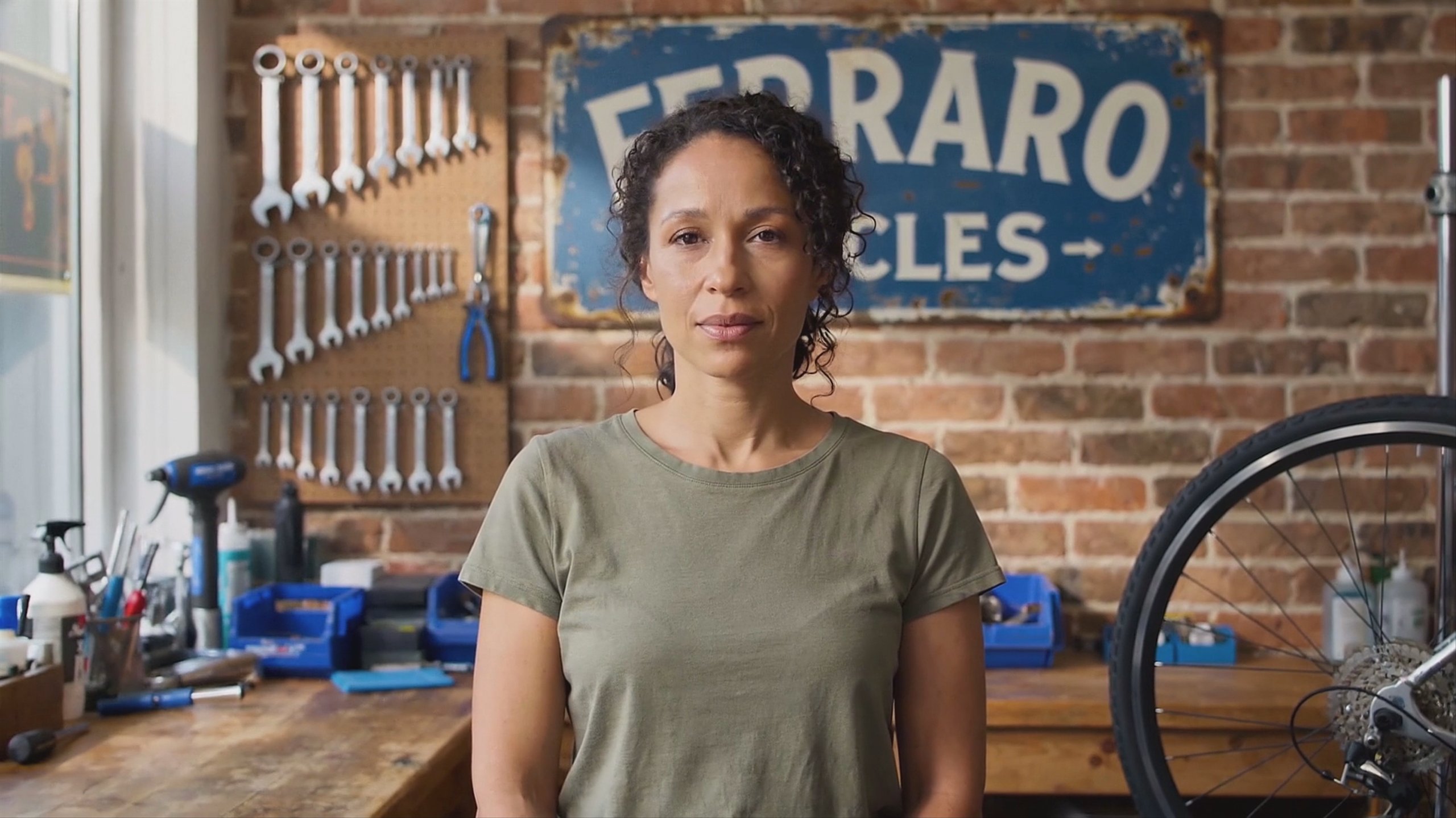 The same clip through a generative upscaler that returned it at 24fps and two pixels wider than 1080p — a woman standing behind the counter of a bicycle repair shop