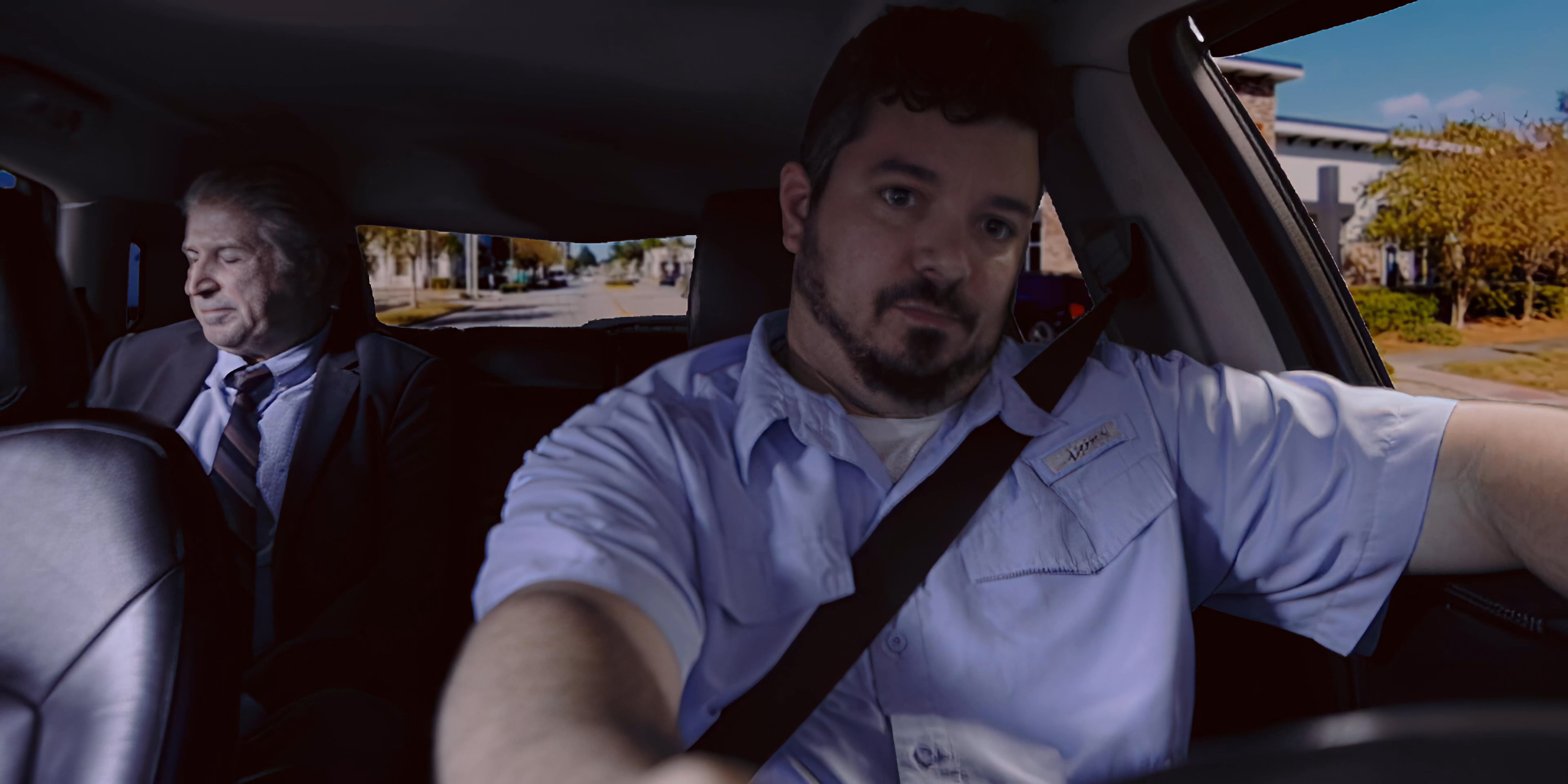 A driver operates a vehicle while transporting a passenger through an urban area during the daytime. The sequence focuses on the professional interaction and the changing scenery visible through the car windows.