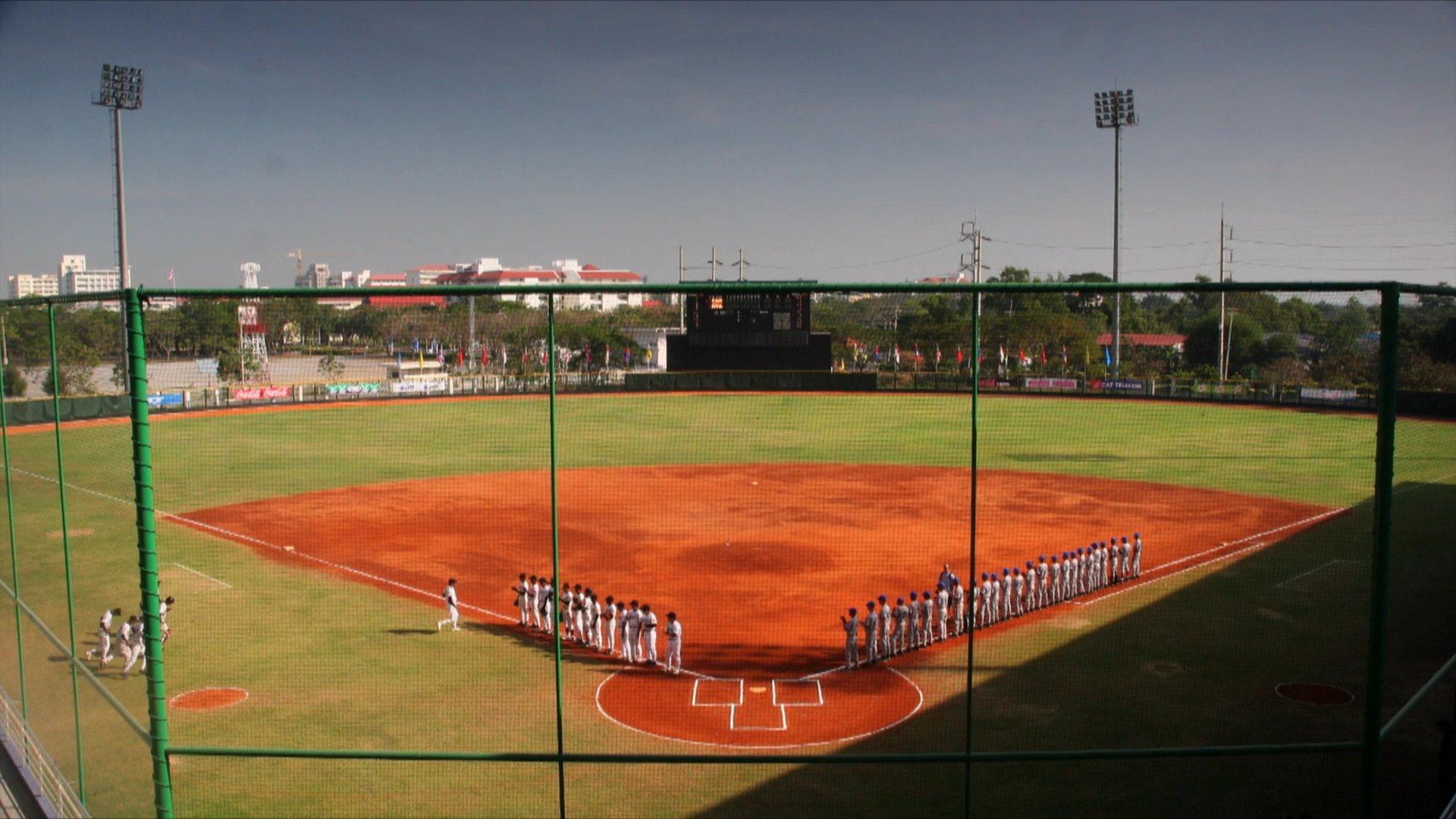 Members of the Cambodia national baseball team line up on the field for a formal pre-game ceremony. Two representatives discuss the event before transitioning to the athletic formation on the diamond.