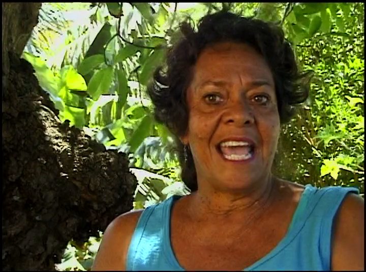 Participants in swimwear receive award boards at an outdoor surf competition event, followed by a woman providing an interview in a tropical outdoor setting.