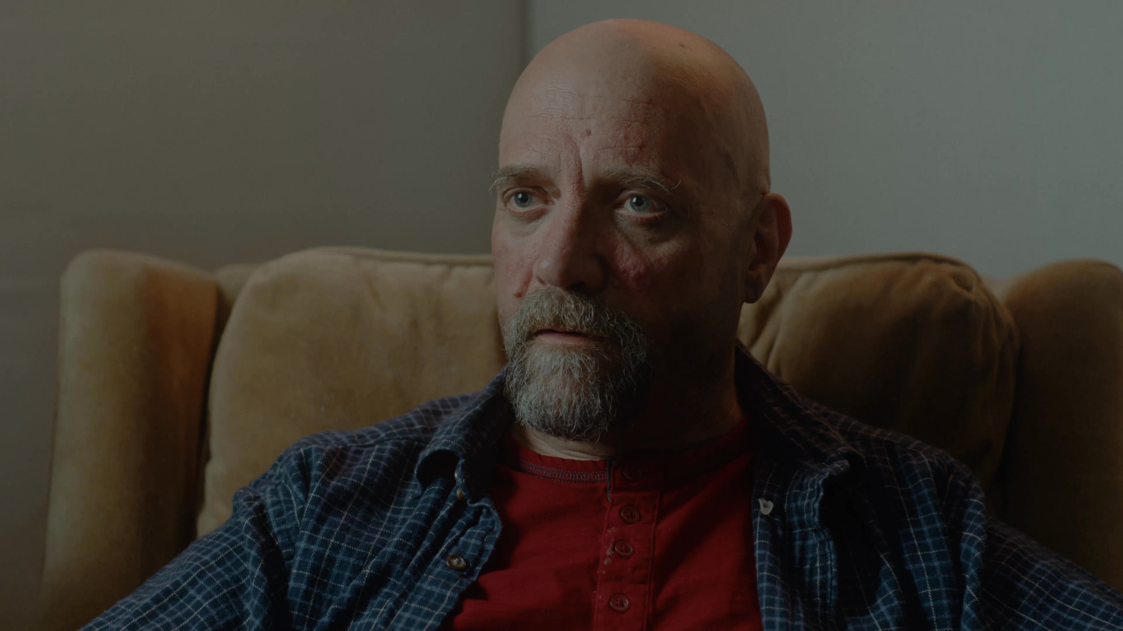 Two men engage in an informal conversation while seated in a living room, alternating focus between their perspectives. The scene captures a quiet, conversational dynamic within a domestic setting.