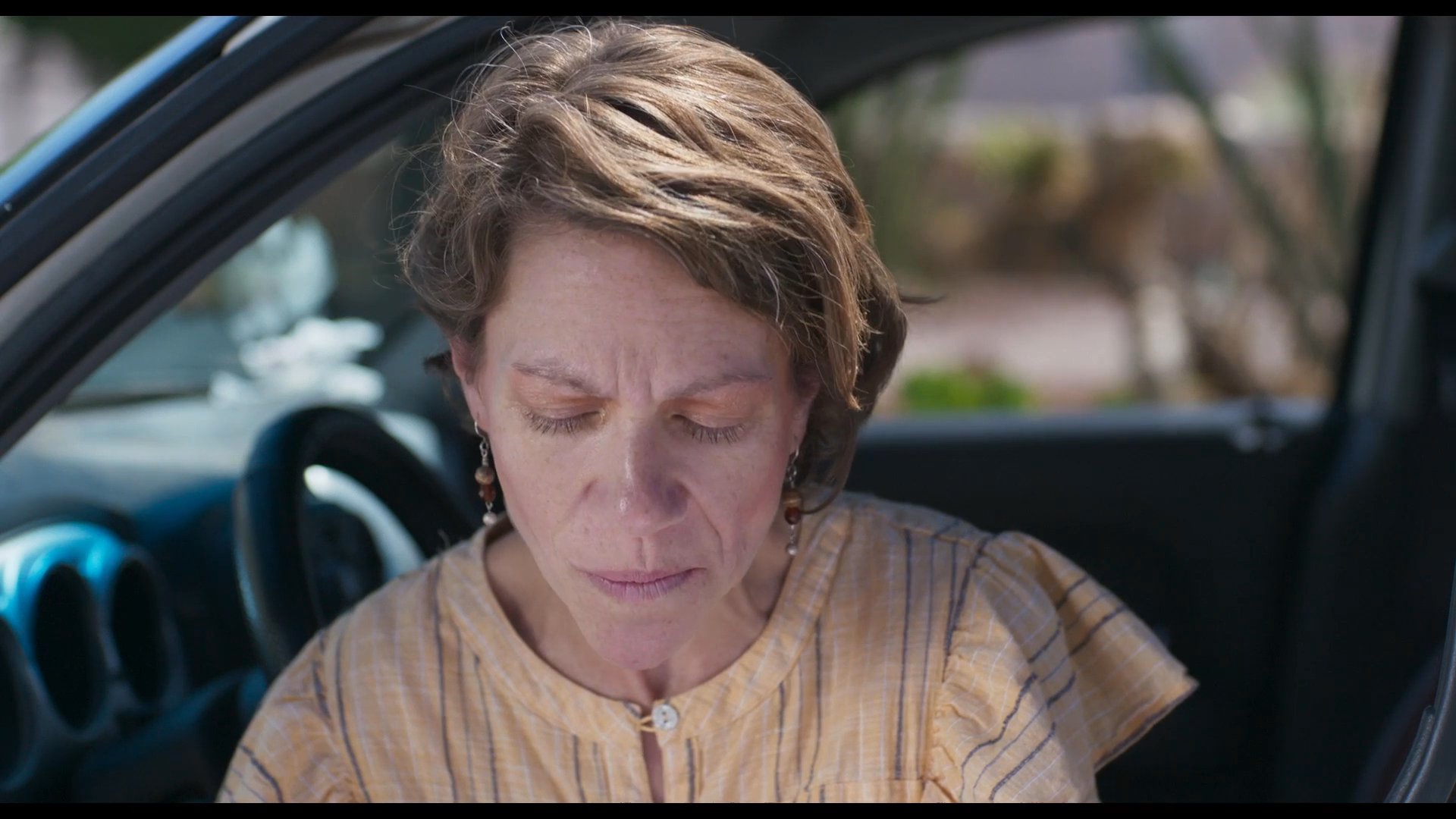 A woman sits inside a parked vehicle, emotionally reading a heartfelt handwritten letter. The intimate sequence focuses on her personal reaction to the poignant message as she reflects on the words.